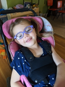 maggie smiling from chair with purple glasses on